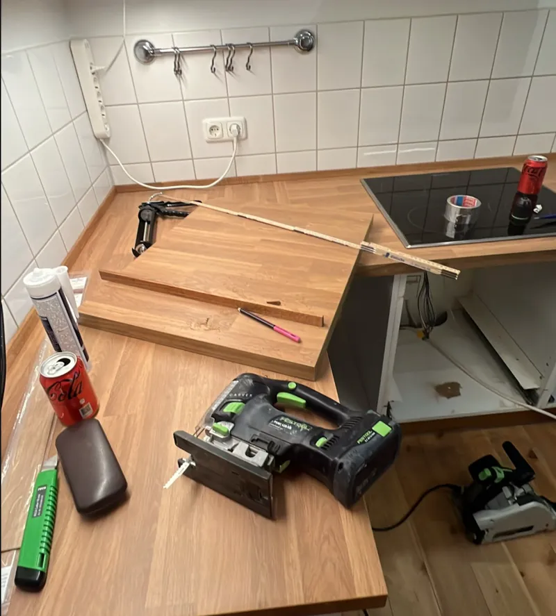 Zuschnitt vor Ort: auf der neuen Eiche-Arbeitsplatte liegen Stichsäge, Zollstock, eine Silikonkartusche und ein abgesägtes Reststück, rechts das bereits eingesetzte Kochfeld.